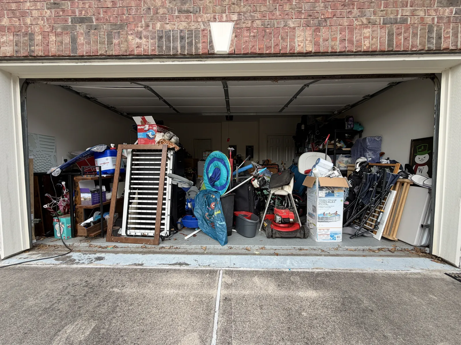 Two-car garage packed wall to wall with furniture, a pool box, a mower and boxes before cleanout